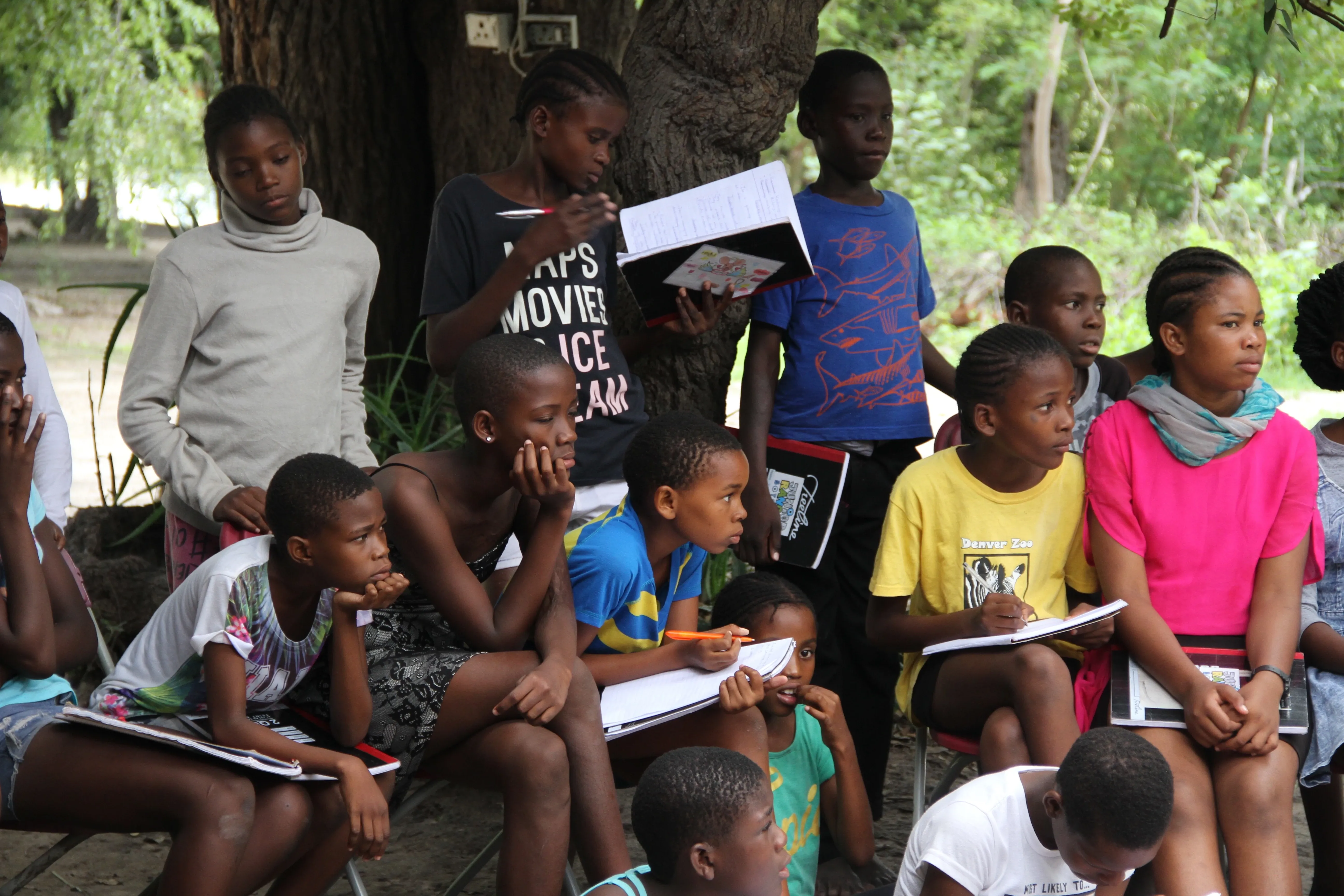 Kinder sitzen draußen mit Heften am Lernen, Botswana