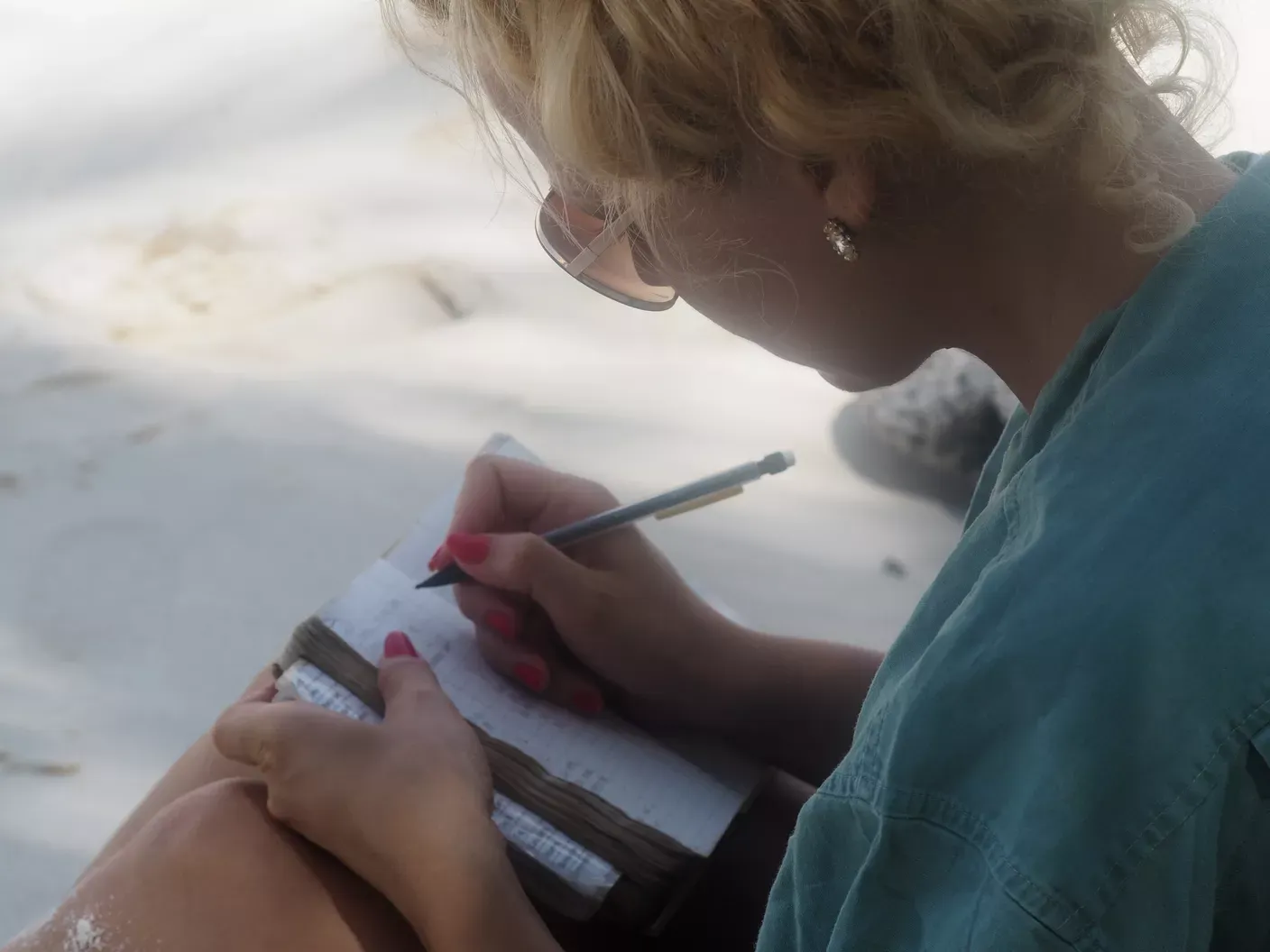 Frau schreibt Notizen in ein Notizbuch und sitzt am Strand