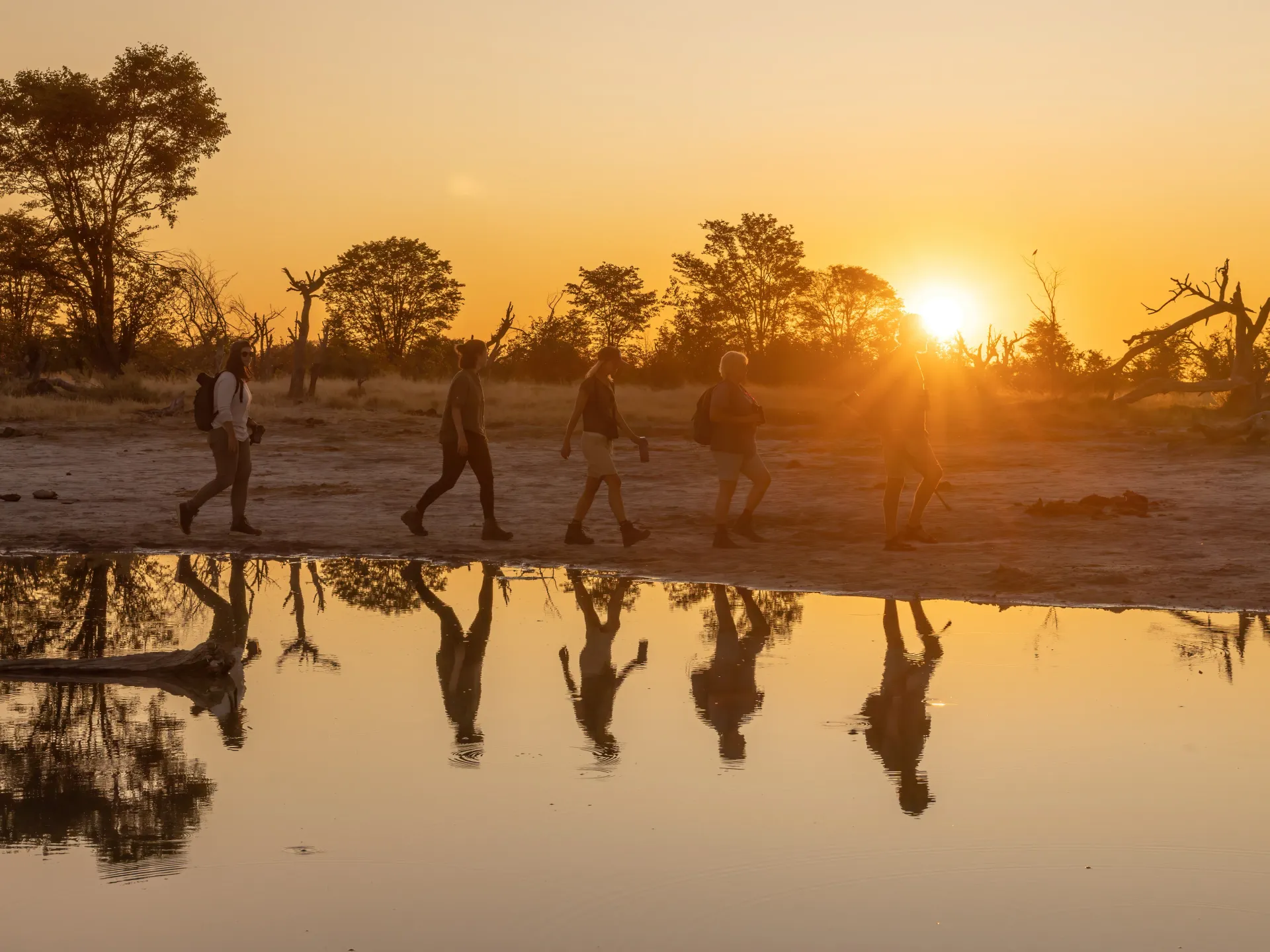 Five people walking close to a waterhole during sunset