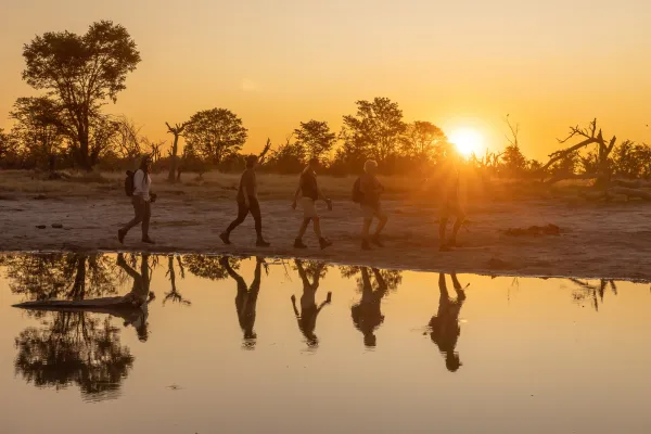 Fünf Menschen, die bei Sonnenuntergang in der Nähe eines Wasserlochs spazieren gehen